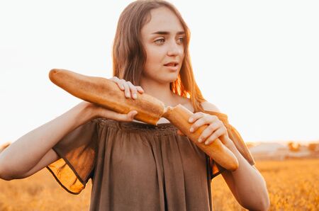 close up view of woman eating french baguette in golden wheat meadowの写真素材