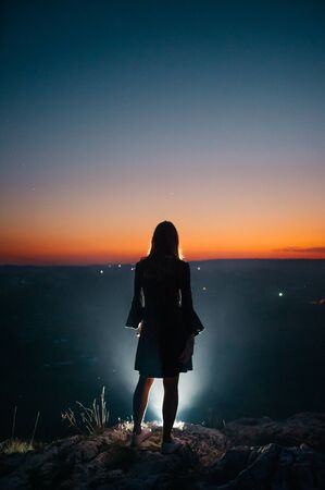 silhouette of a young woman in dress above night cityの写真素材