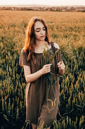 woman in green dress stands smilling in wheat field with shining sunの写真素材