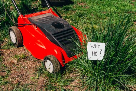 close up view of electric lawn mower cutting a bush with a sign why me