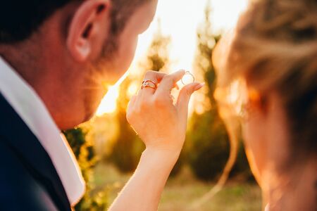 newlyweds holding a wedding ring onn the sunset backgroundの写真素材