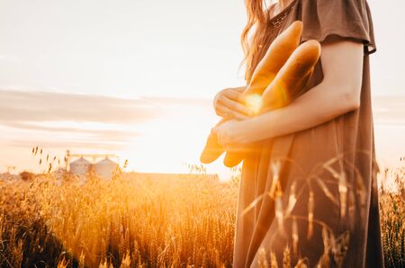 woman holds freshmade french baguette in wheat field during sunrise in countrysideの写真素材