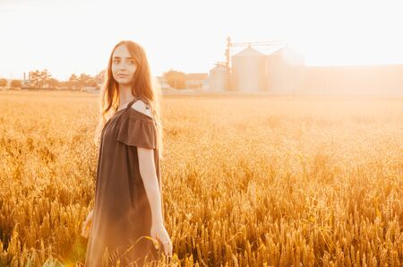 woman in green dress stands smilling in wheat field with shining sunの写真素材