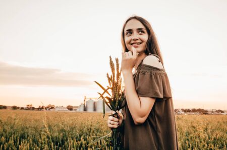 happy woman in green dress smiles in wheat fieldの写真素材