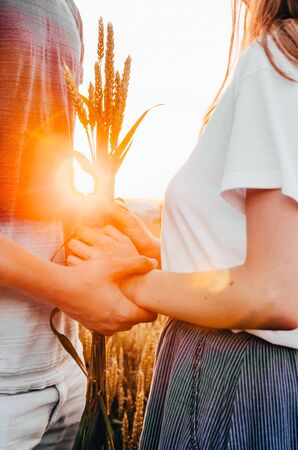 a young couple standing close and holding hands in wheat field while sunsetの写真素材