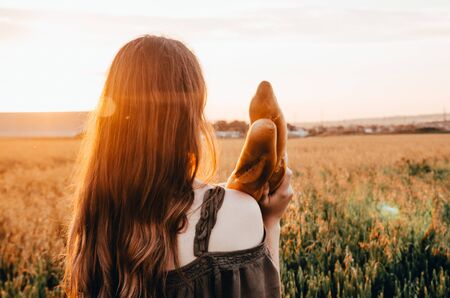 woman holds freshmade french baguette in wheat field during sunsetの写真素材