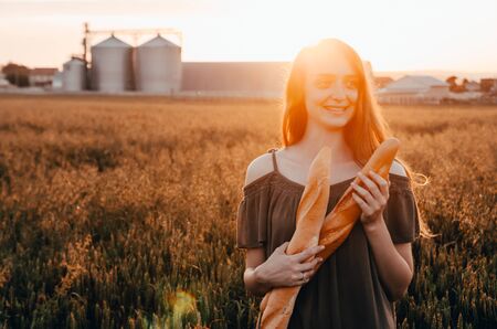 woman in dress holds freshmade french baguettes in green wheat fieldの写真素材