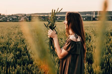 close up photo of happy woman in dress standing in green wheat fieldの写真素材