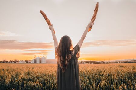 woman in dress holds freshmade french baguettes in green wheat fieldの写真素材