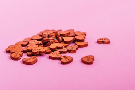 tiny wooden hearts with love written on them isolared on pink background. symbol of love concept
