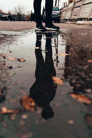 reflection of man standing near the puddle. autumn season outdoors with fallen leavesの写真素材