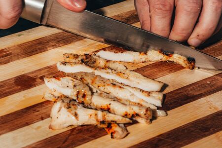 cooker in black uniform cutting grilled chicken breast