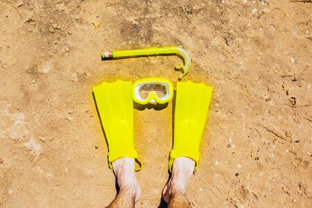 yellow swimming flippers on the legs with mask and tube on sand beachの写真素材