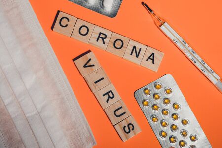 Novel coronavirus disease written with wooden letters. breathing mask, thermometer and pills on orange background. symptoms of the virus "2019-nCoV"の写真素材