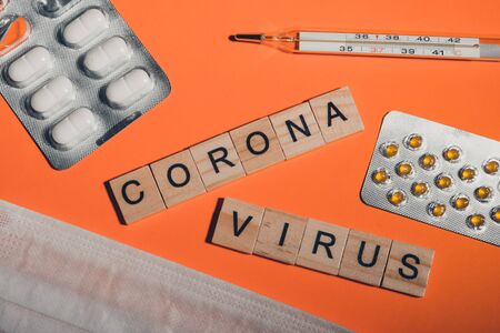Novel coronavirus disease written with wooden letters. breathing mask, thermometer and pills on...