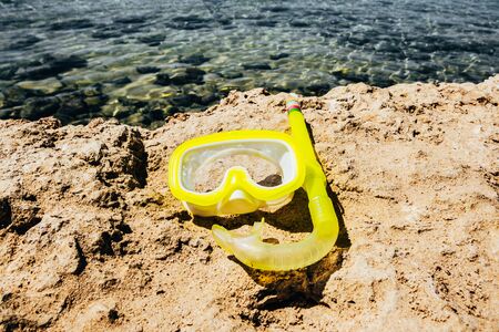 yellow swimming mask with tube on stones by the sea. waves hitting the sea shoreの写真素材