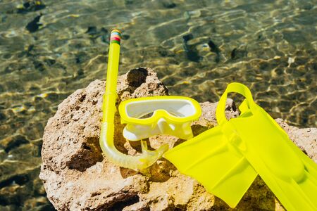 yellow swimming flippers with face mask on big stone by the seaの写真素材