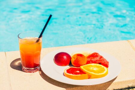 orange cocktail and plate of sliced fruits near the pool