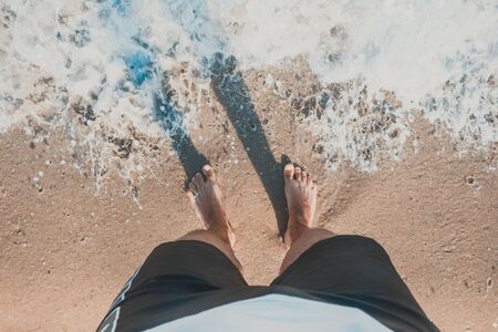 Close-up of a man's bare feet walking on the beach , with the edge of the wave foaming softly under them, tinted colorsの写真素材