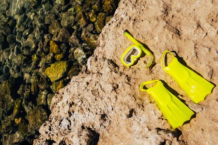 yellow swimming flippers with face mask on big stone by the seaの写真素材
