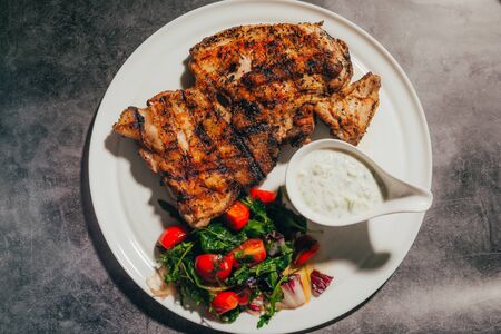 Grilled pork chop steak with fresh vegetable salad and sauce on plate . Top view .の写真素材