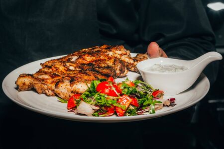 Grilled pork chop steak with fresh vegetable salad, tomatoes and sauce on plate in chef hand .の写真素材