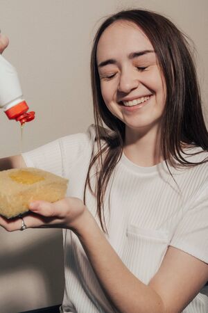 laughting girl in a white t-shirt pours dishwashing liquid on a yellow spongeの写真素材