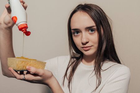 girl watch in camera  in a white t-shirt pours dishwashing liquid on a yellow spongeの写真素材