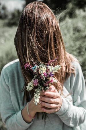 a woman with wildflowers bouquet posing and  hides his face behind long hair to remain unknown  .の写真素材
