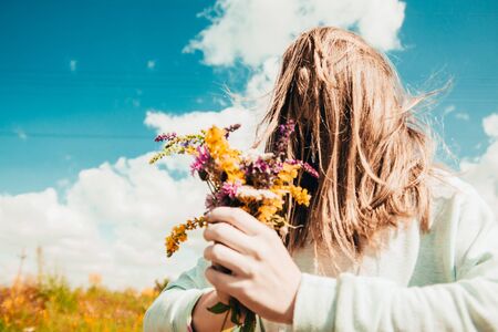 a woman with wildflowers bouquet hides his face behind long hair to remain unknown  .の写真素材