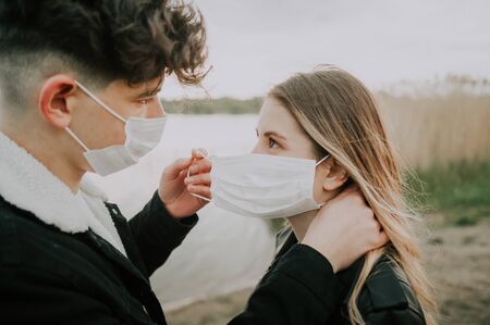 couple taking care of each other to protect from virus. man putting on medical mask on his girldfriend faceの写真素材