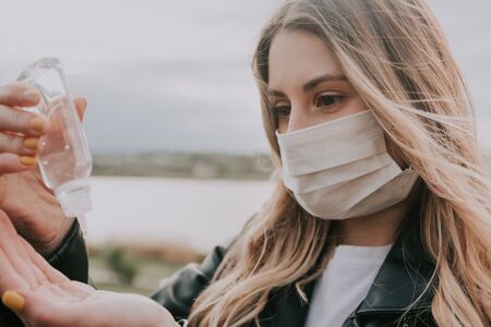 young woman in mask using hand sanitizer gel outside to prevent the spread of virus and epidemic diseaseの写真素材