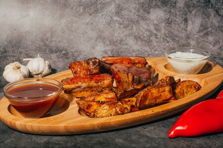 Roasted ribs and grilled potato with two sauces  , served on big wooden plate . restaurant menu .の写真素材