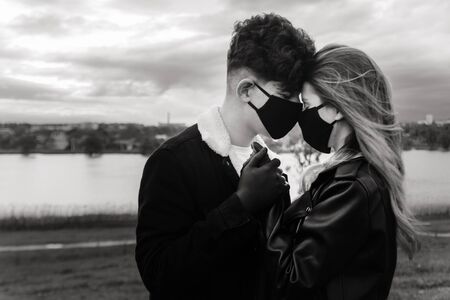 a couple in black masks and gloves hold hands and look at each other . love in quarantine . selective focus . black and white .の写真素材