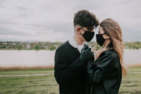 a couple in black masks and gloves hold hands and look at each other . love in quarantine . selective focus .の写真素材