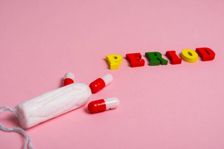 word PERIOD made of multi colored wooden letters near the cotton tampon and red pills . menstruation time concept .の写真素材