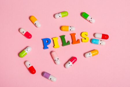 word PILLS made of wood letters.  multi colored tablets on which a smiley is drawn around the word .の写真素材