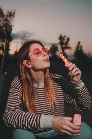 woman blowing soap bubbles and sitting on the scooter. summer fun activities  .の写真素材