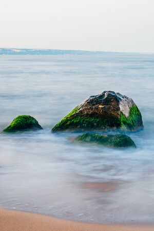 wide view of  sand beach with big rocks covered with moss . longexposure