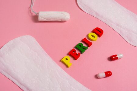 word PERIOD made of multi colored wooden letters near the cotton tampon and red pills . menstruation time concept .の写真素材