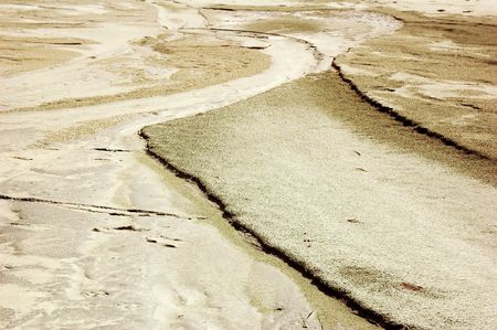 A river cuts across a beach making for the ocean, carving patterns in the golden sand.の写真素材