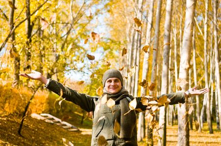 Young man having fun throwing up piles of autumn leaves .