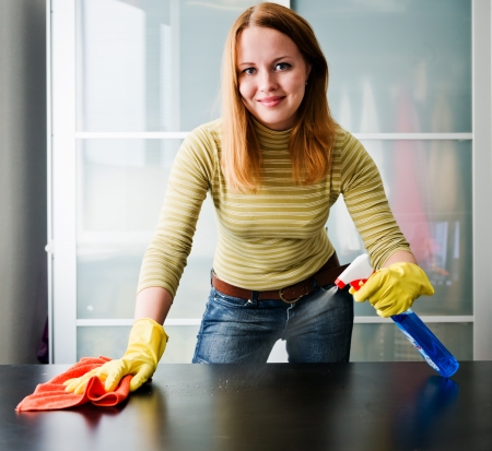 Happy girl cleaning table with furniture polish at home の写真素材