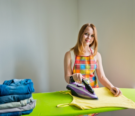 Young beautiful woman ironing clothes in room on grey background の写真素材
