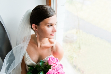 Young beautiful bride waits for groom near the window の写真素材