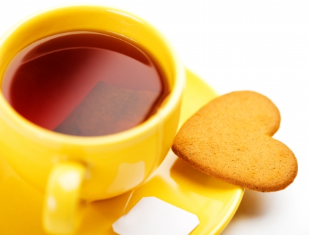 yellow cup with tea bag and heart-shaped cookie isolated on white の写真素材