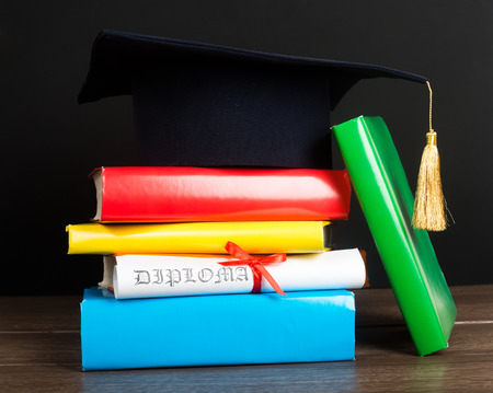 A mortarboard and graduation scroll, tied with red ribbon, on a stack of booksの写真素材