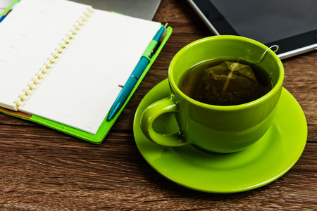 Office desk with laptop computer, planner, cup of teaの写真素材