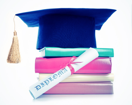 A mortarboard and graduation scroll, tied with red ribbon, on a stack of booksの写真素材