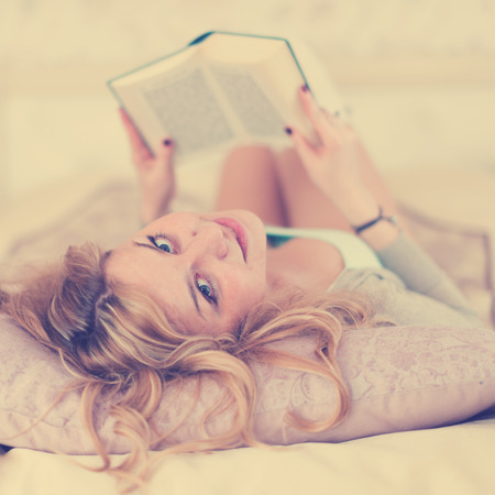 Beautiful woman reading on a bed relaxing turning to give the camera a beaming smile.の写真素材